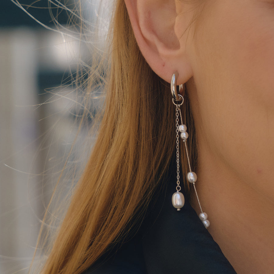 silver-finish asymmetric pearl-style tassel earring worn on ear
