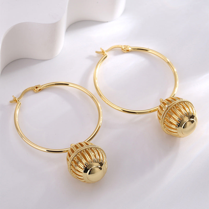 gold plated caged orb charm hoop earrings arranged in studio
