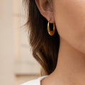 model wearing gold plated wavy oval hoop earrings