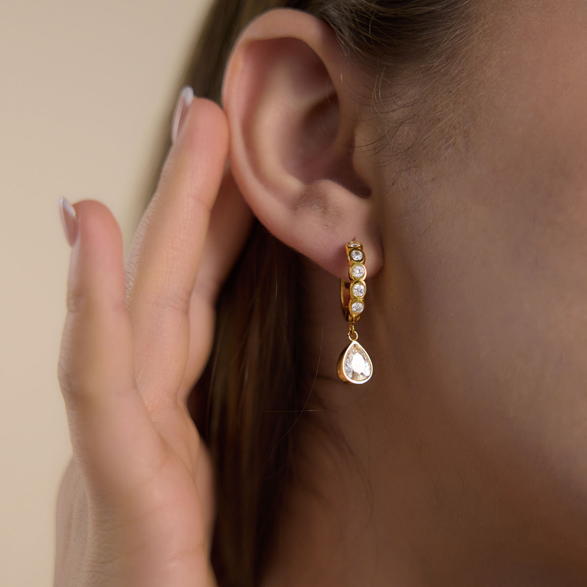 Gold tone teardrop charm huggie shown on the ear