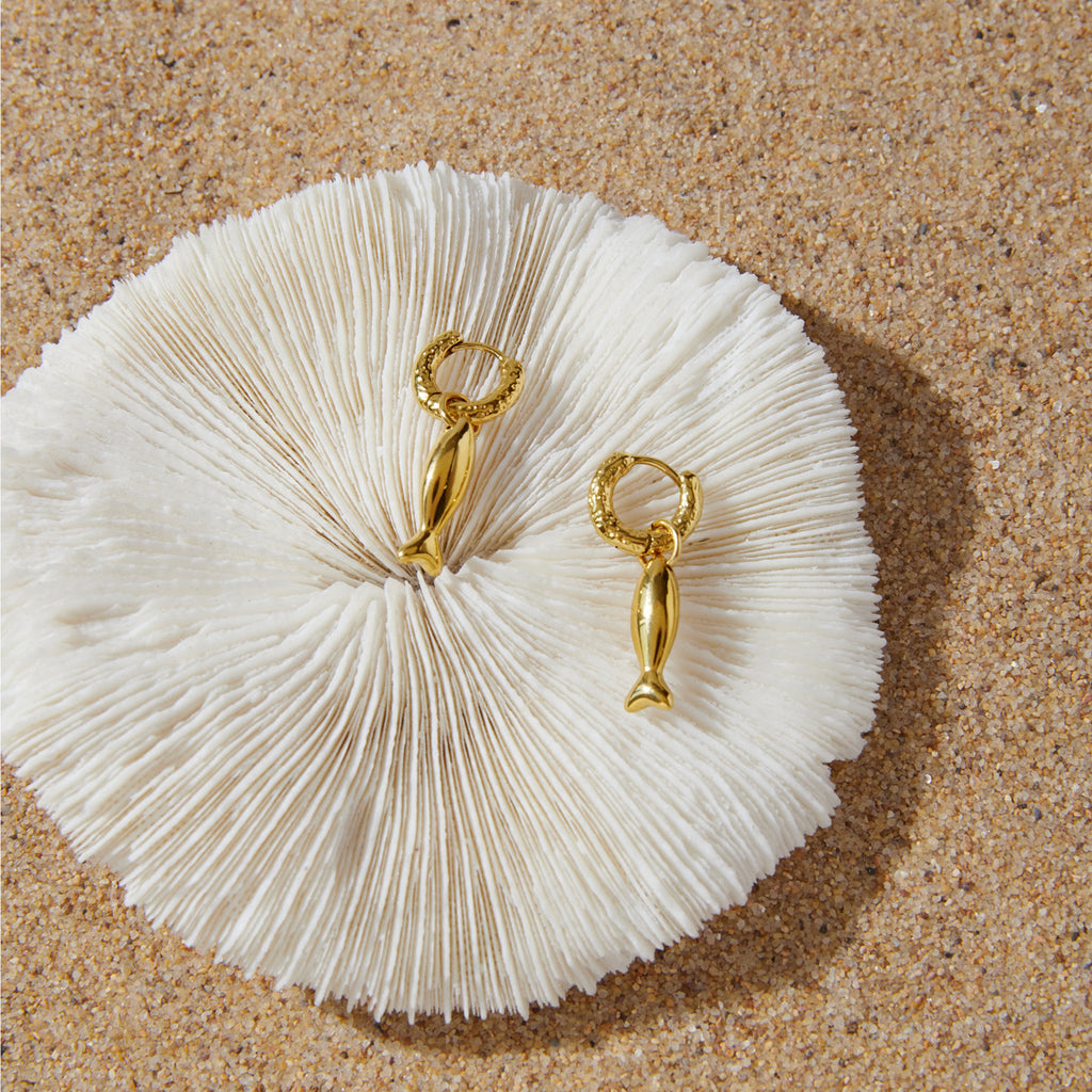 Fish charm hoop earrings arranged on white textured surface