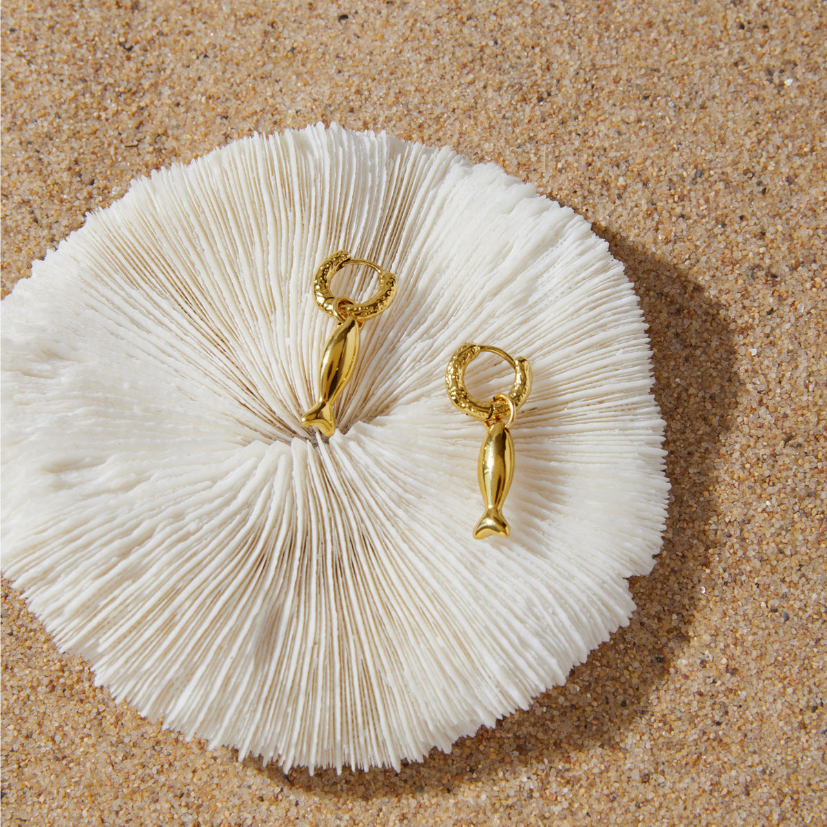 Fish charm hoop earrings arranged on white textured surface