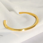 angled view of slim gold plated open bangle on satin