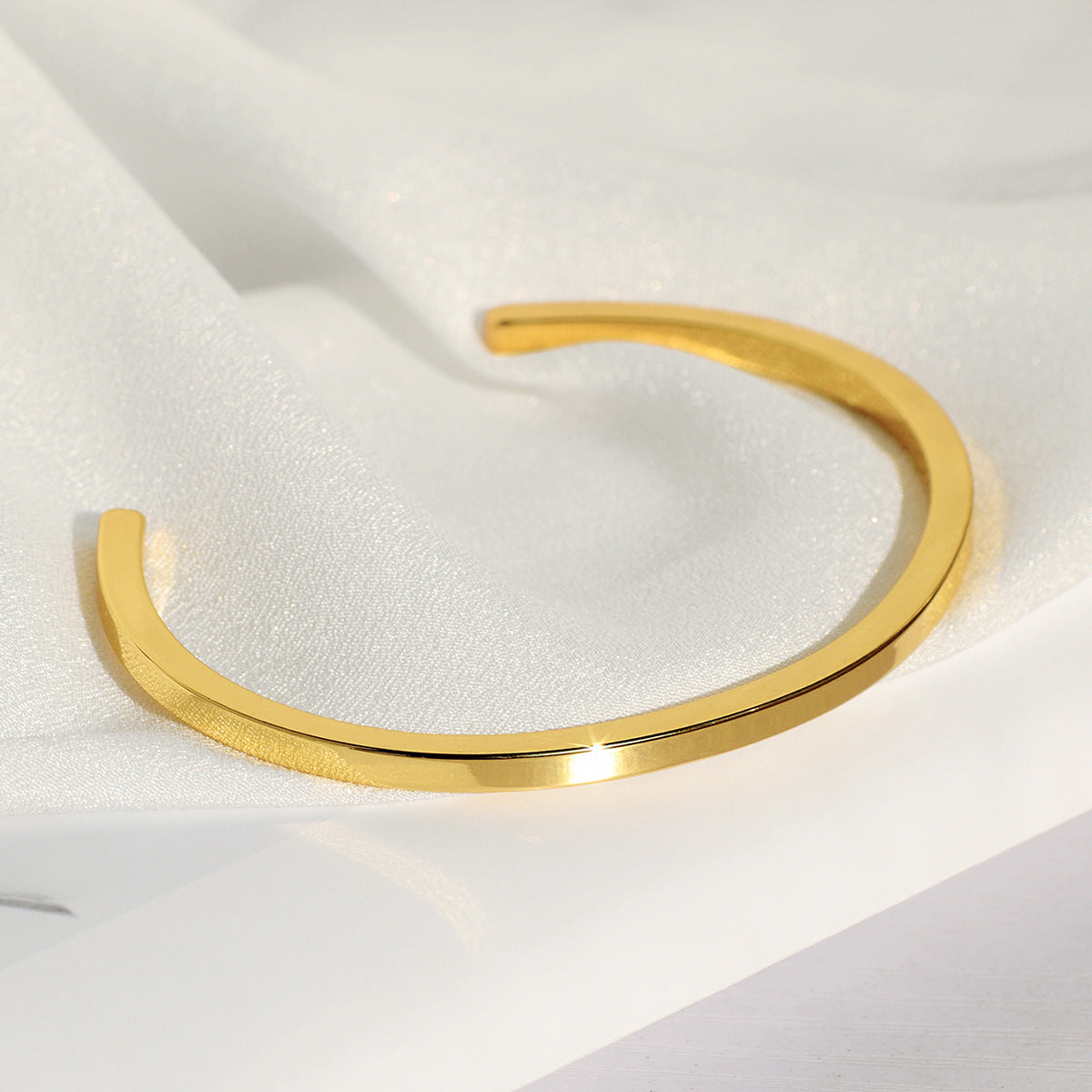 angled view of slim gold plated open bangle on satin