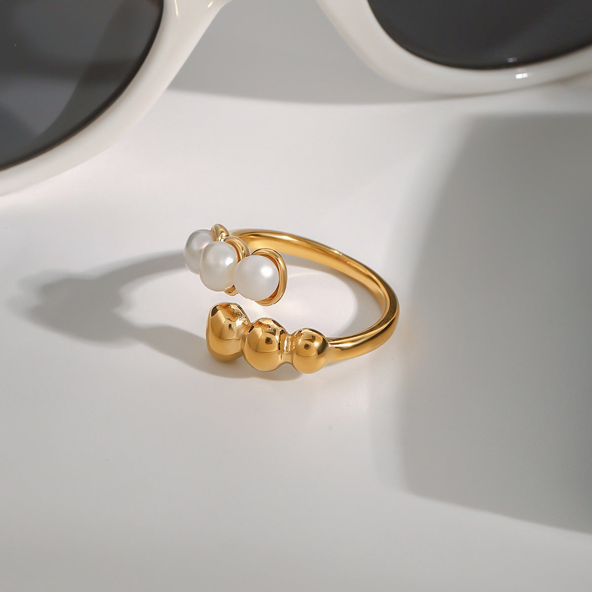 Three white beads facing three polished balls on the open ring