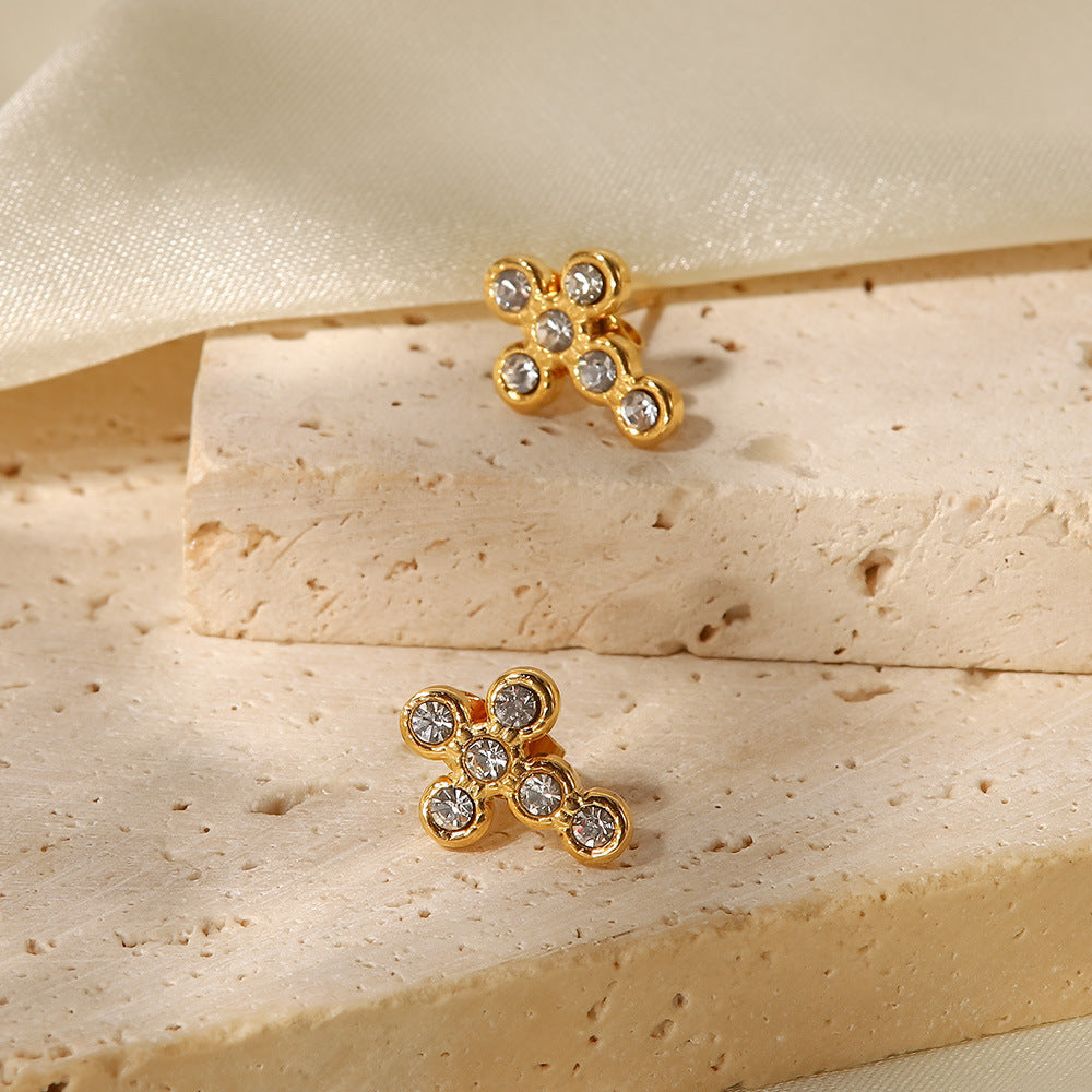 Clear round accents in gold-tone cross studs beside a stone block