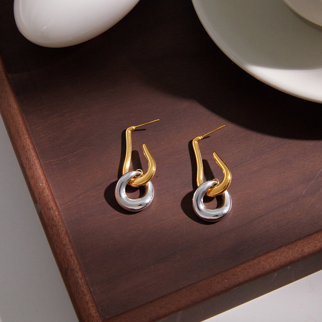 two-tone sculptural drop earring pair on a dark wood surface