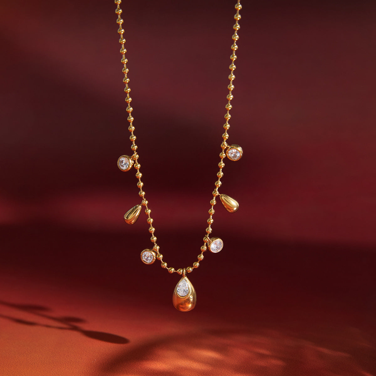 teardrop and clear-stone station necklace against red backdrop