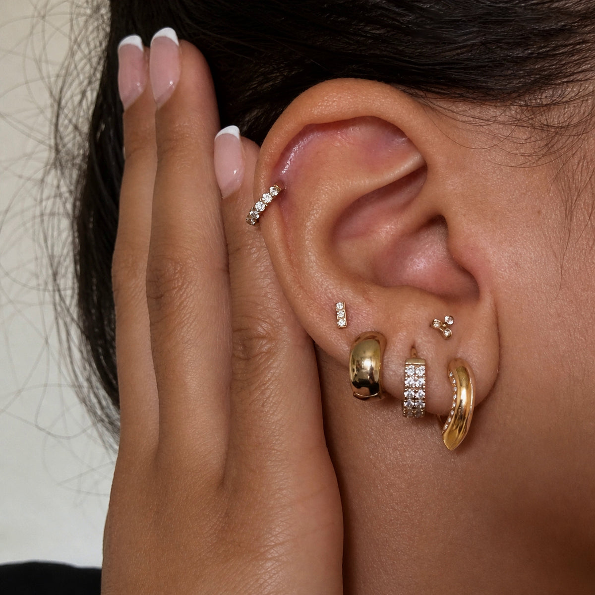 Gold-tone U earrings and small hoops shown in an ear stack