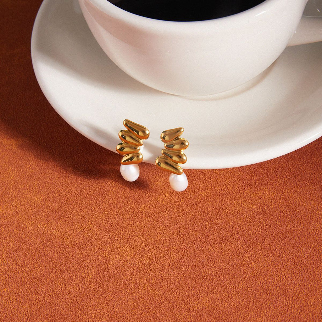 Gold-tone cluster earrings beside a cup