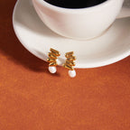 Gold-tone cluster earrings beside a cup