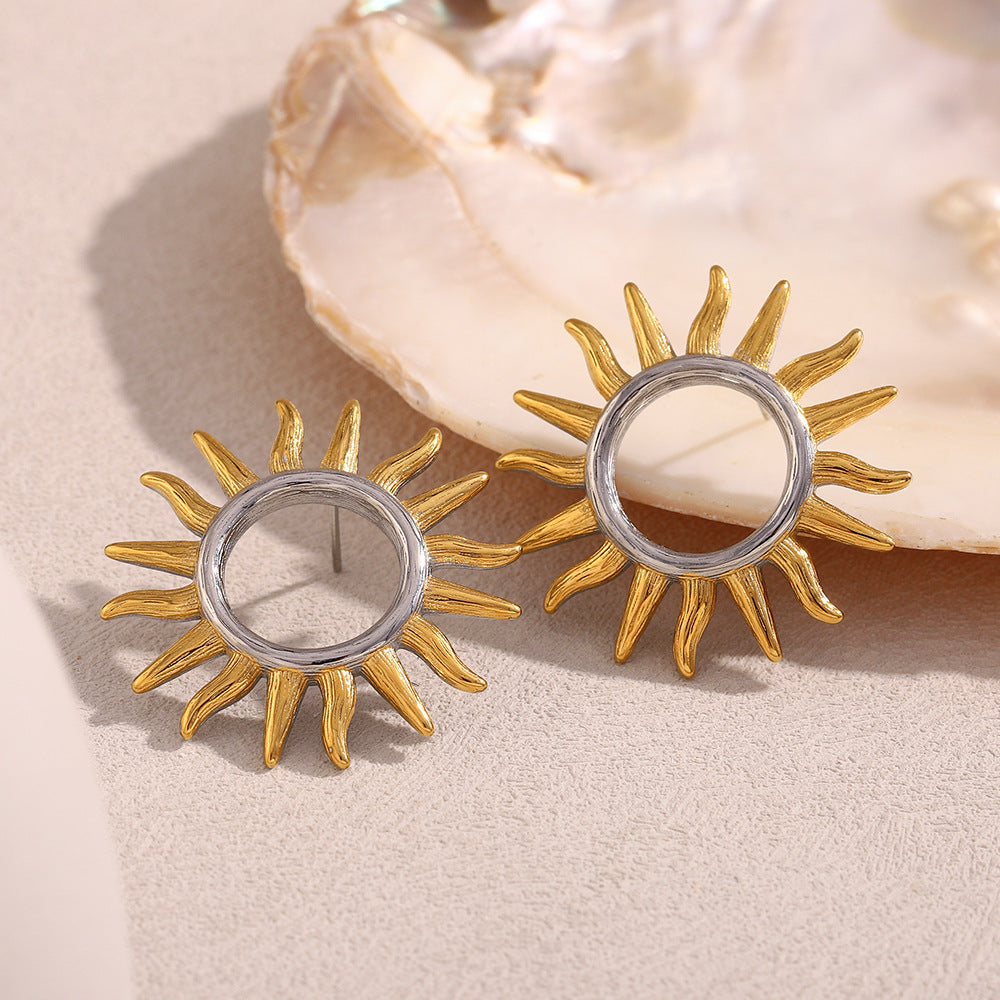 two-tone hollow sunburst stud earrings beside a shell