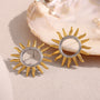 two-tone hollow sunburst stud earrings beside a shell