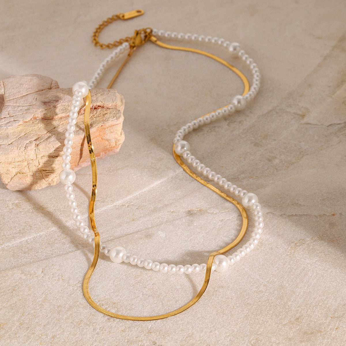 White bead strand and gold flat chain layered on a stone display