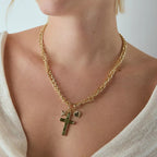 Gold-tone stainless steel cross pendant necklace with green accents worn on a model
