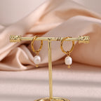 small gold plated pearl drop hoops displayed on an earring stand