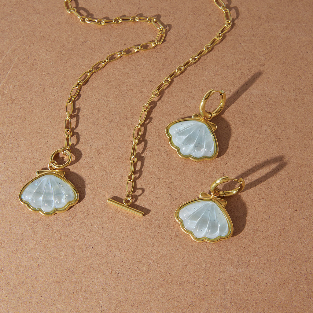 Pale blue shell necklace and hoop earrings arranged on sand