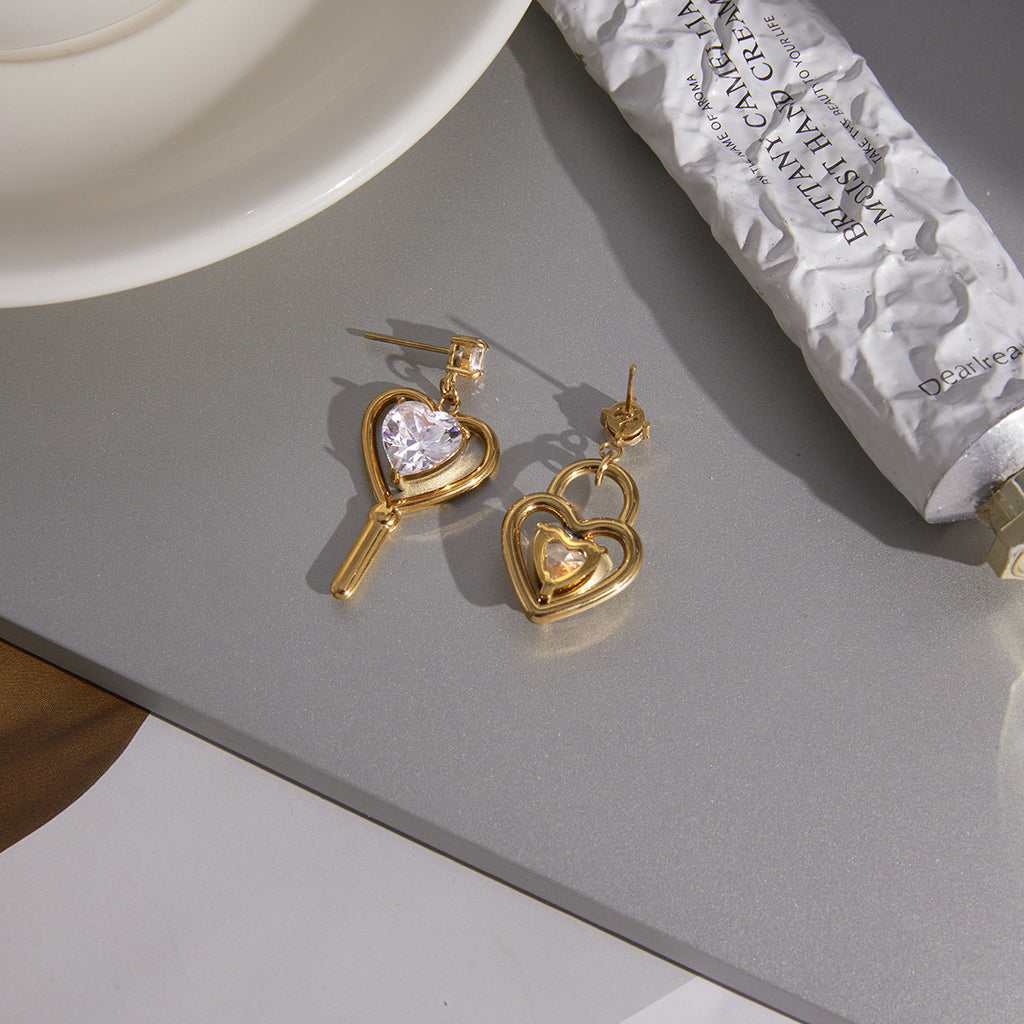 asymmetric clear-stone heart earrings on a neutral surface