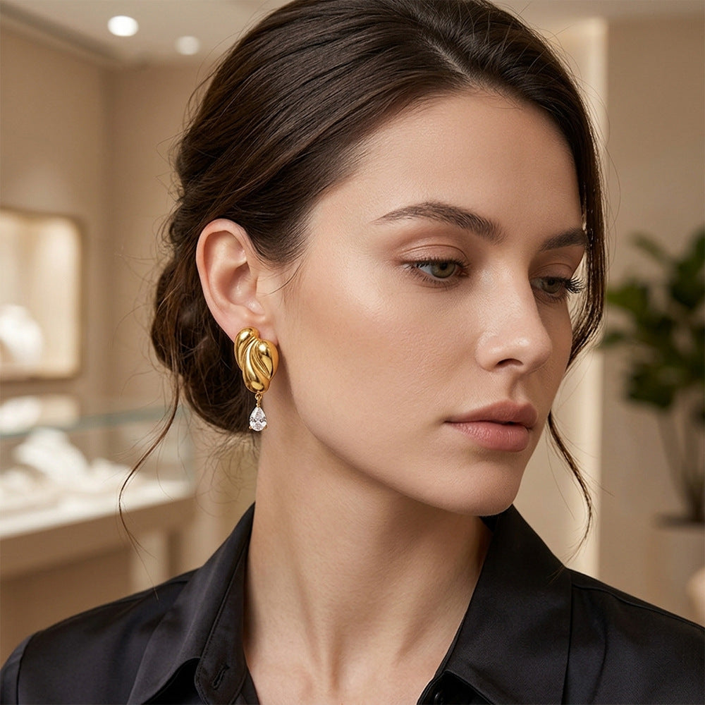 Gold tone sculptural fold earrings with teardrops worn on model
