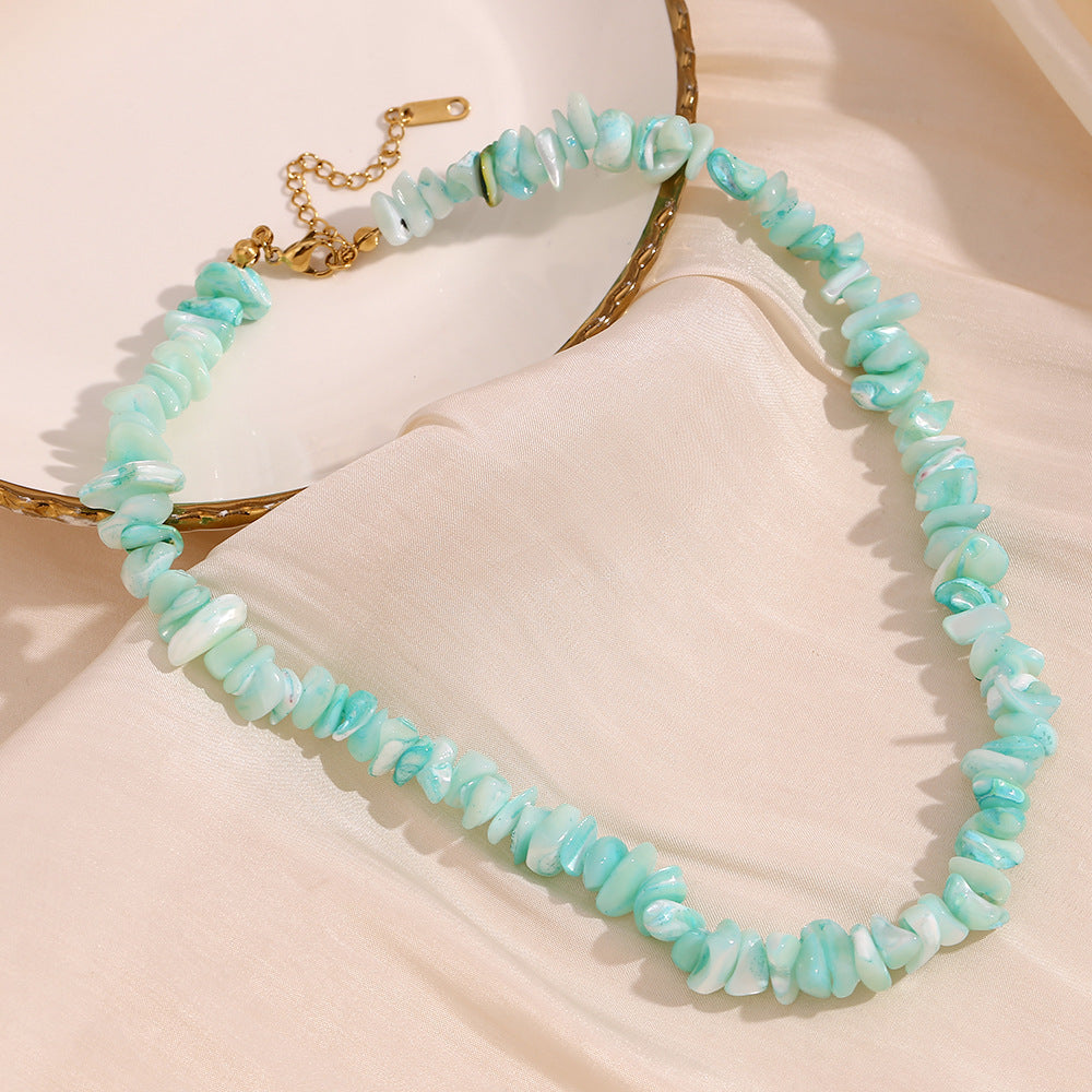 Aqua stone chip necklace with gold tone clasp displayed beside a dish