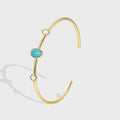 gold plated open cuff with turquoise-color oval and pale stones on gray