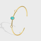gold plated open cuff with turquoise-color oval and pale stones on gray