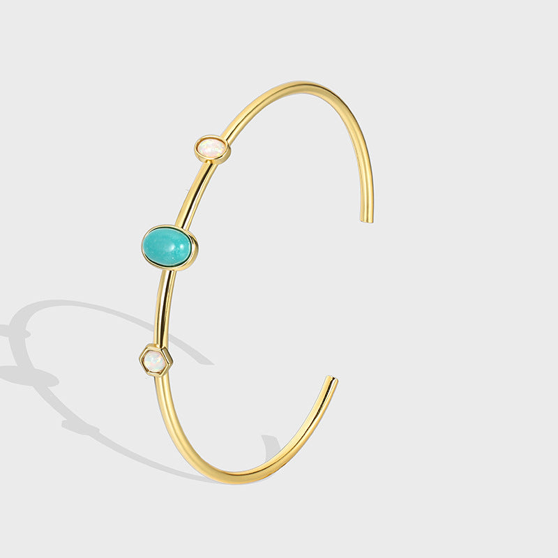 gold plated open cuff with turquoise-color oval and pale stones on gray