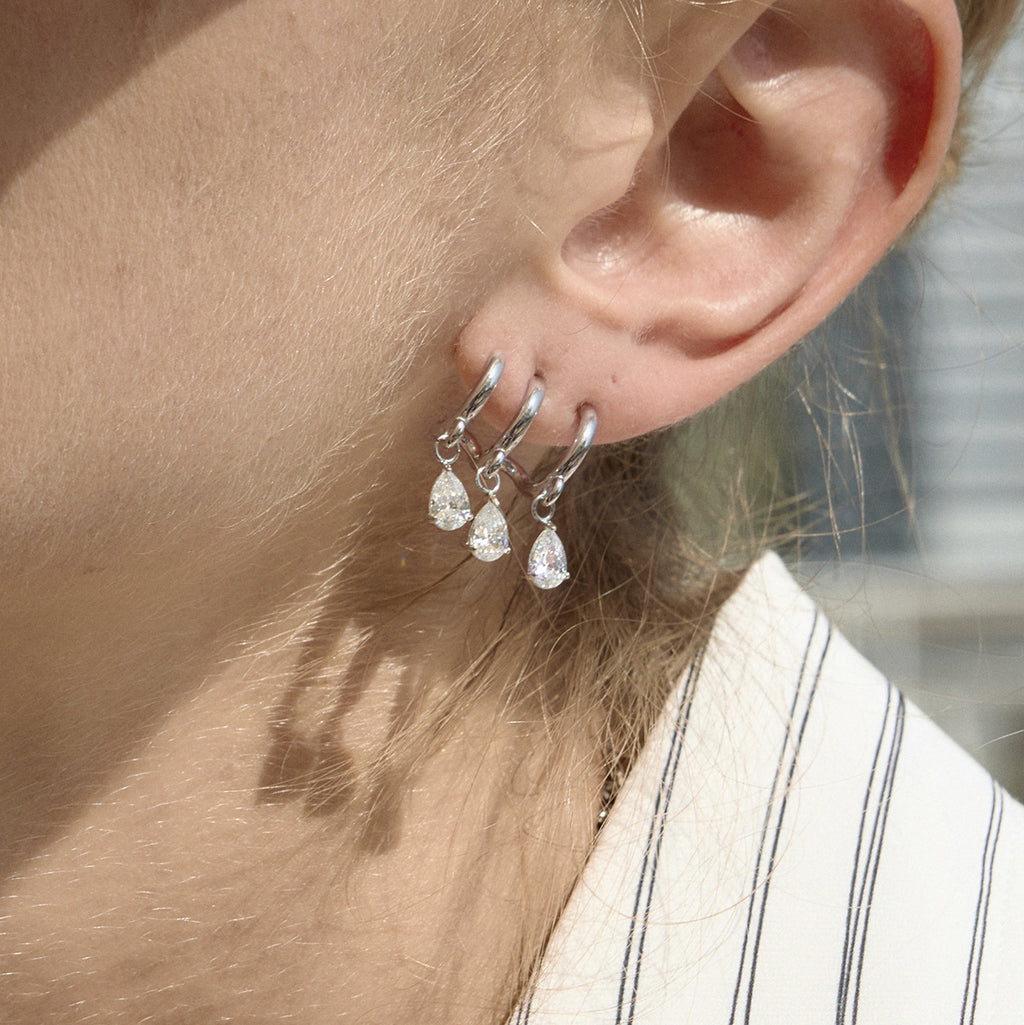 Silver-tone triple-curve earring with pear-shaped drops worn close-up