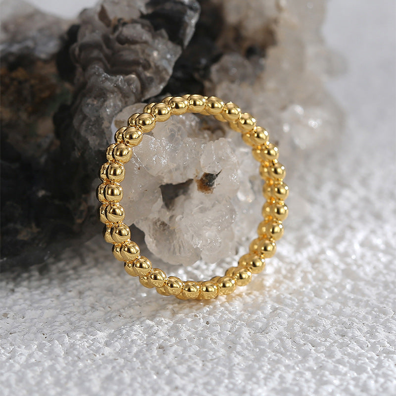 gold plated beaded ring standing against a mineral display