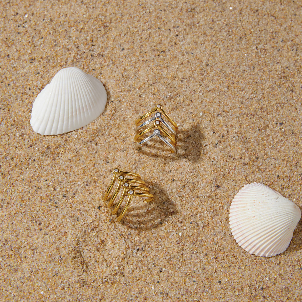 Two open chevron rings displayed on sand with shells