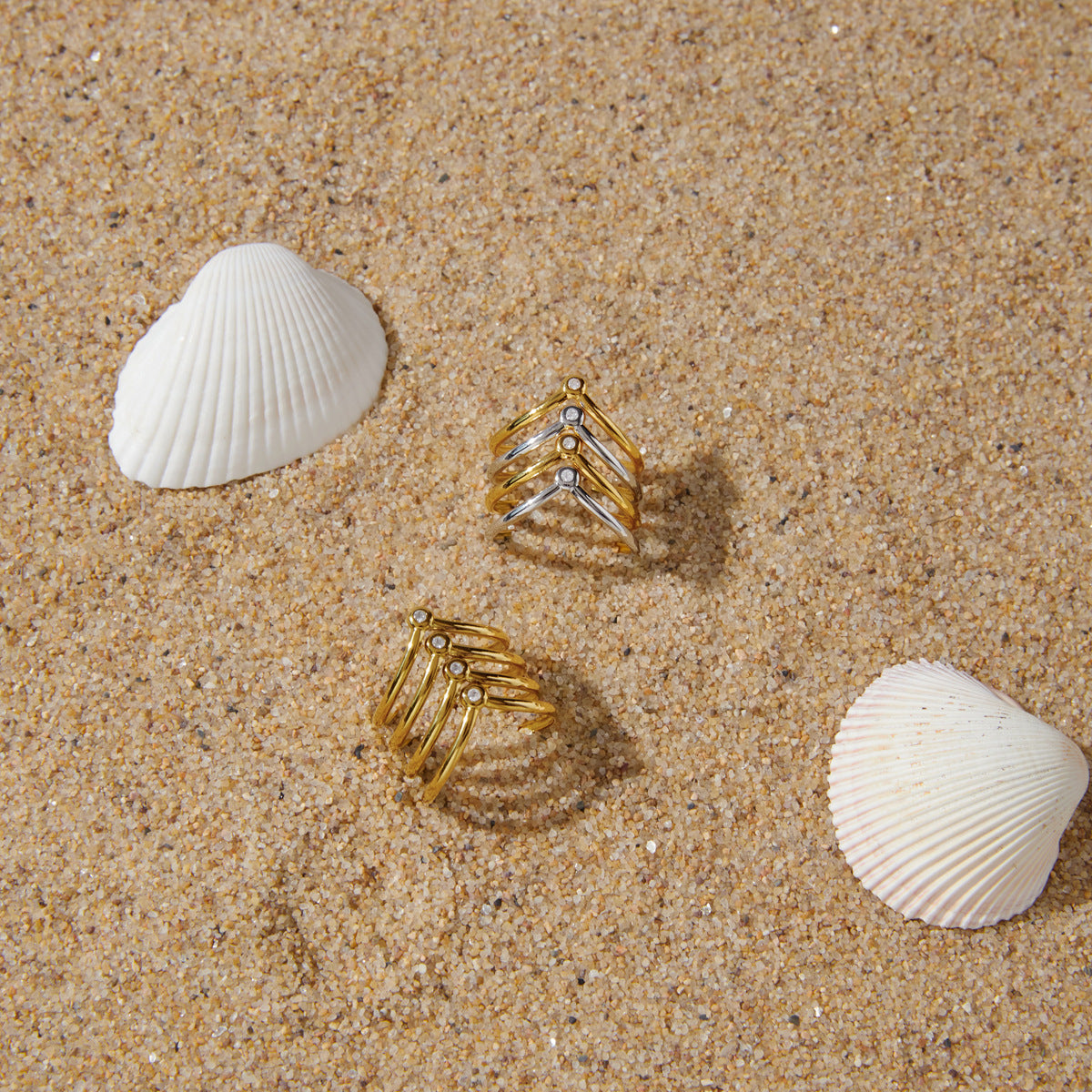 Two open chevron rings displayed on sand with shells