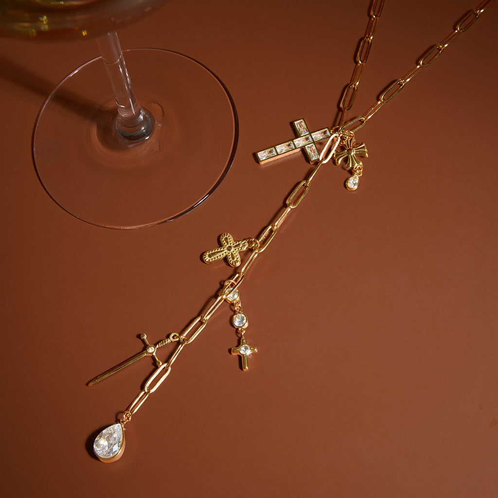 cross charm Y necklace styled on a warm reflective surface