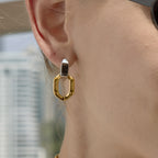 Two-tone angular oval drop earring close-up on ear