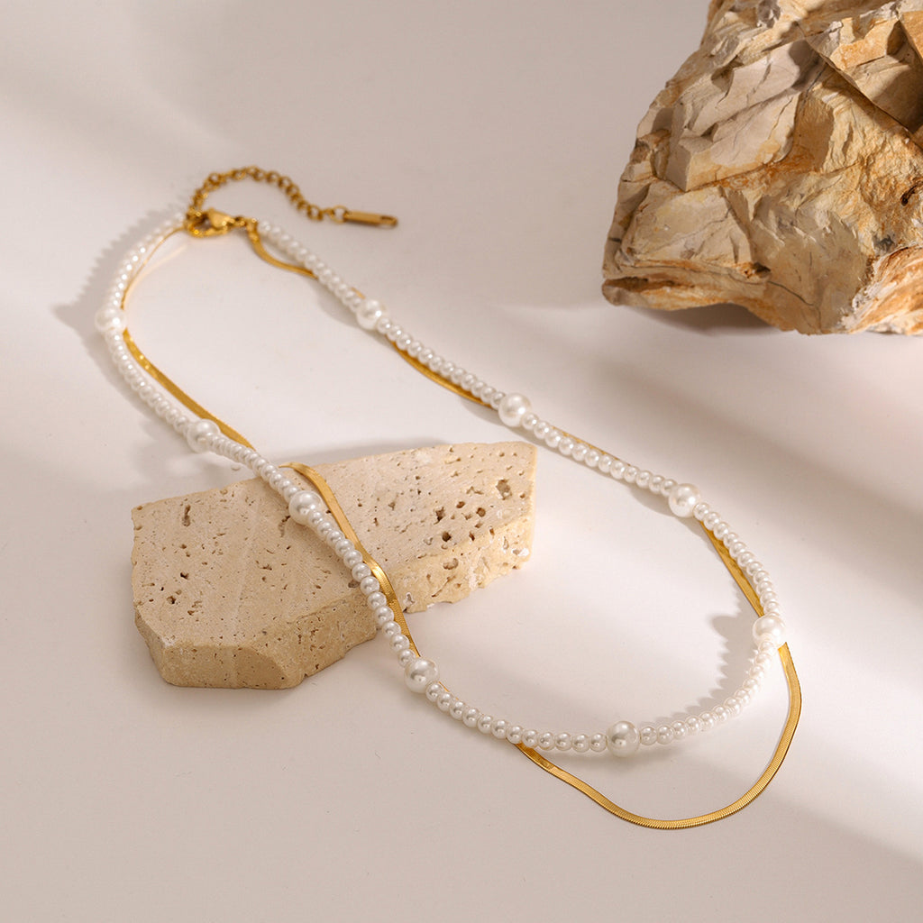 Layered bead and chain necklace arranged beside a stone block