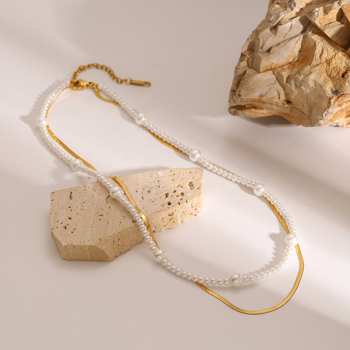 Layered bead and chain necklace arranged beside a stone block