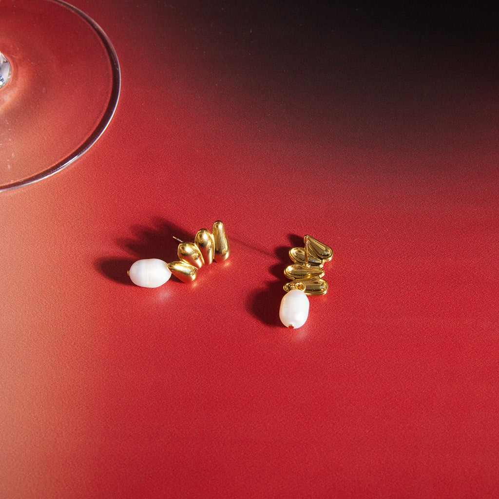 Pearl drop earrings arranged beside a glass