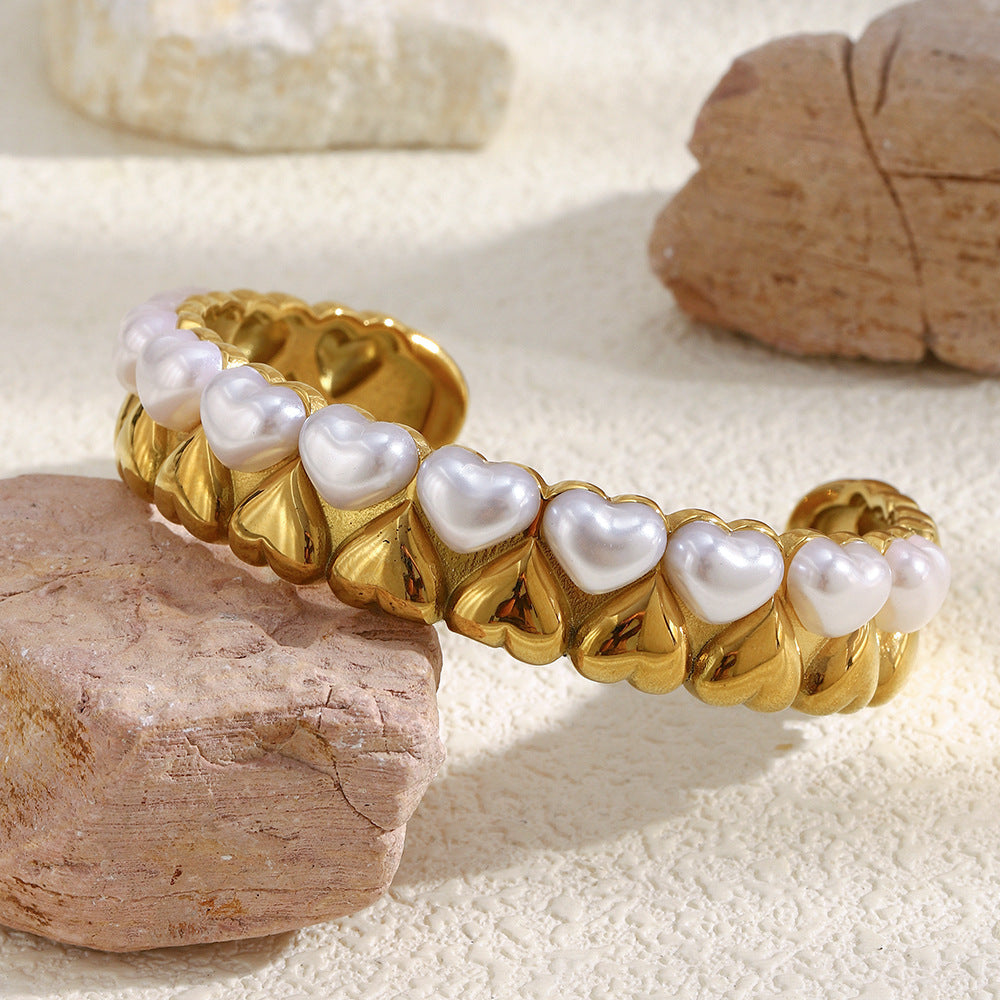 angled front view of sculptural gold plated heart cuff on stones