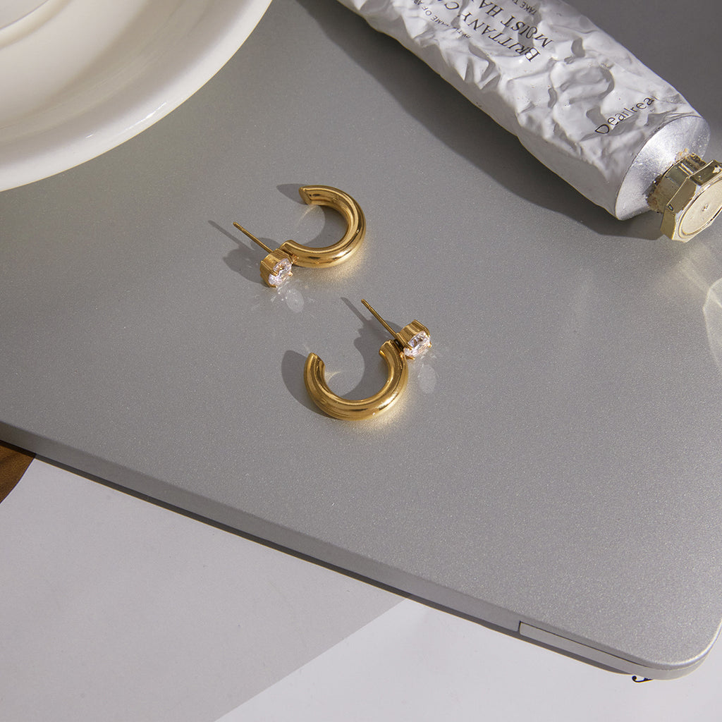 gold plated clear stone C-hoop earrings on a gray surface