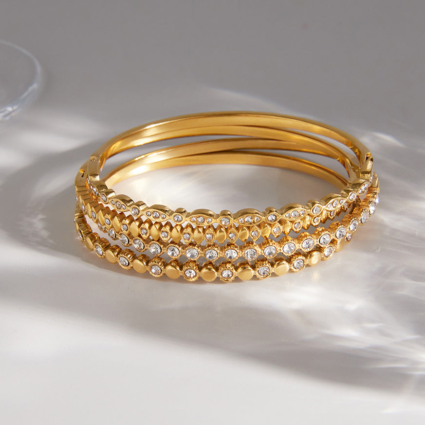 Four slim gold-tone stainless steel bangles with varied clear accent rows