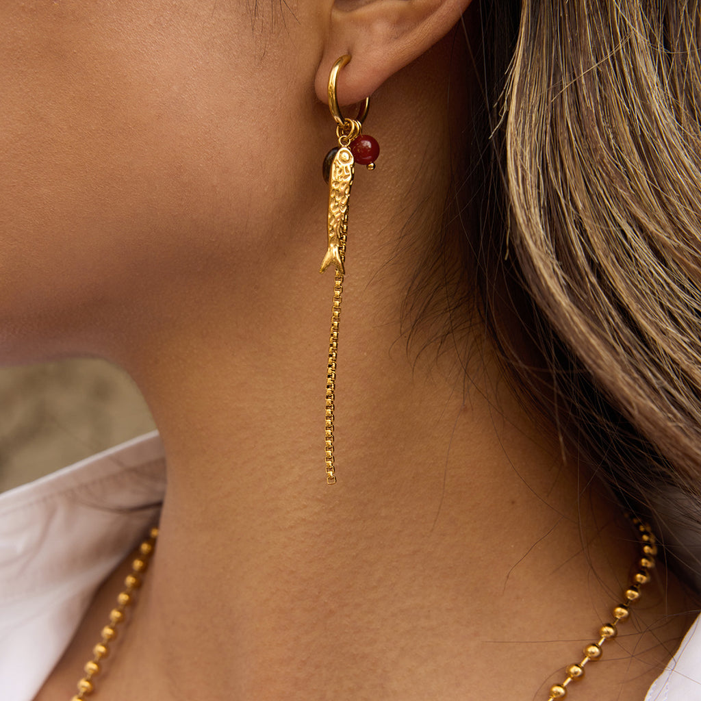 fish charm and chain tassel earring worn on ear