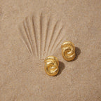 Textured stainless steel knot earrings on sand