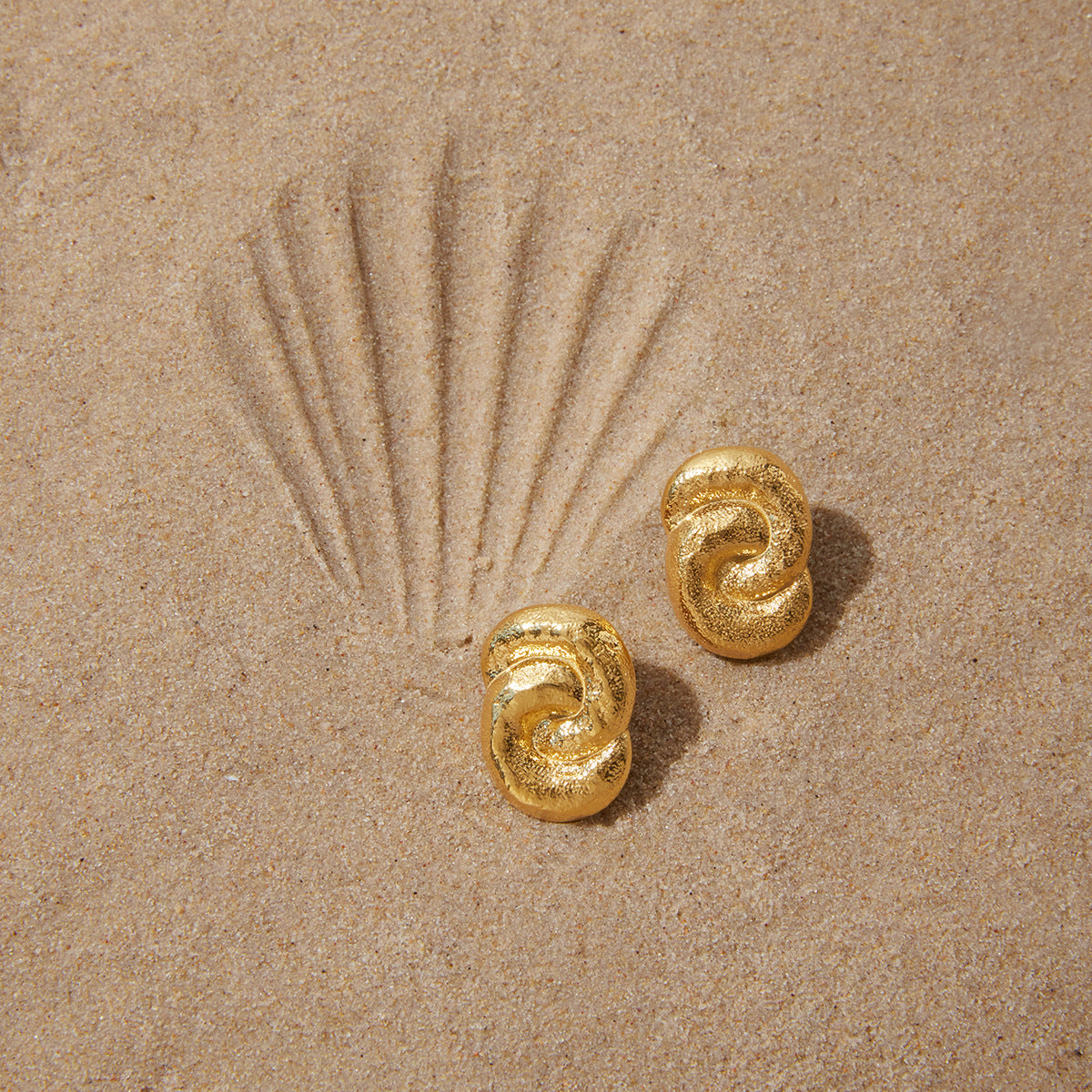 Textured stainless steel knot earrings on sand