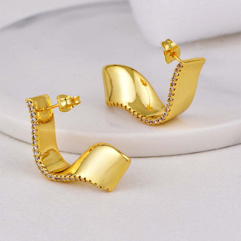 gold plated folded ribbon clear stone stud earrings in a standing studio view