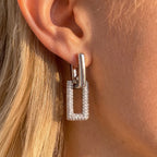 Silver tone rectangular rhinestone drop worn on an ear