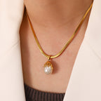 White bead pendant with a flowing gold-tone cap worn on a flat chain
