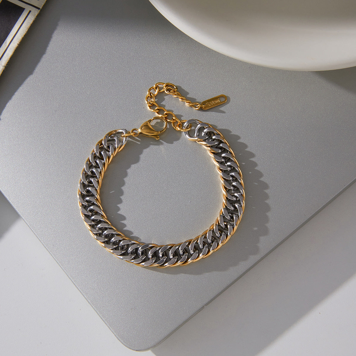 gold plated and silver-finish Cuban chain bracelet on gray surface