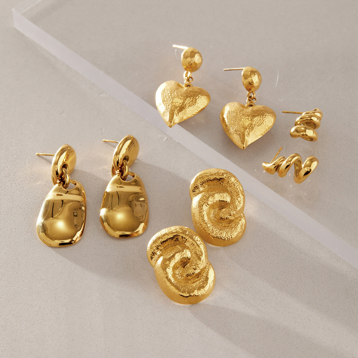 Several sculptural gold-tone earrings on a neutral surface