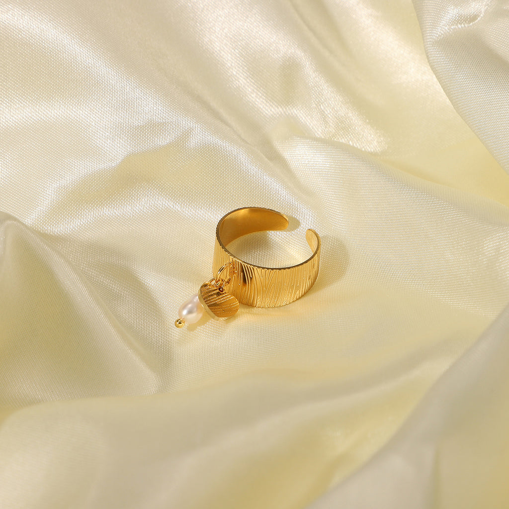 Gold plated textured open ring with a heart charm and white drop bead on cream fabric
