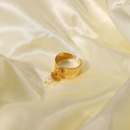 Gold plated textured open ring with a heart charm and white drop bead on cream fabric