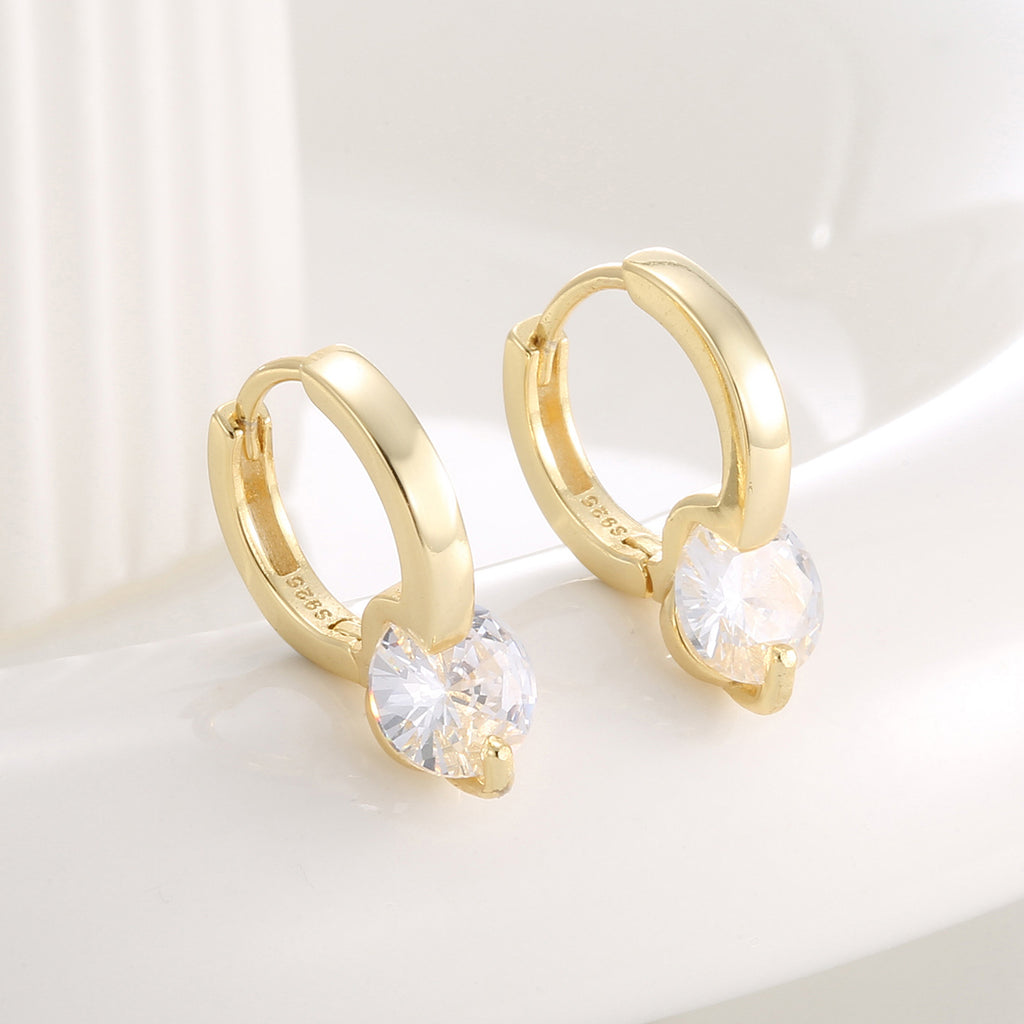 angled pair of round zirconia huggie earrings on a pale surface
